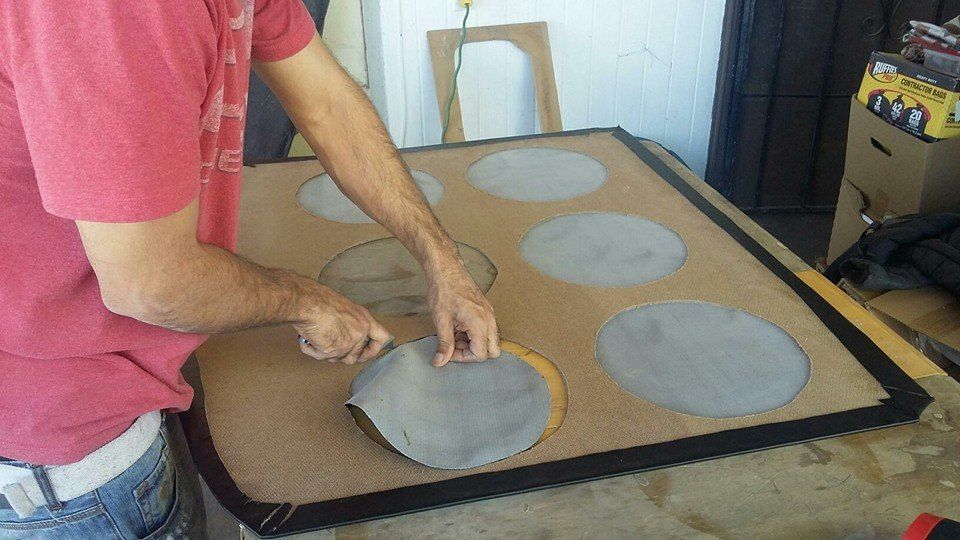 A person cutting a gray circle from a larger sheet of material. The material has several circle outlines.