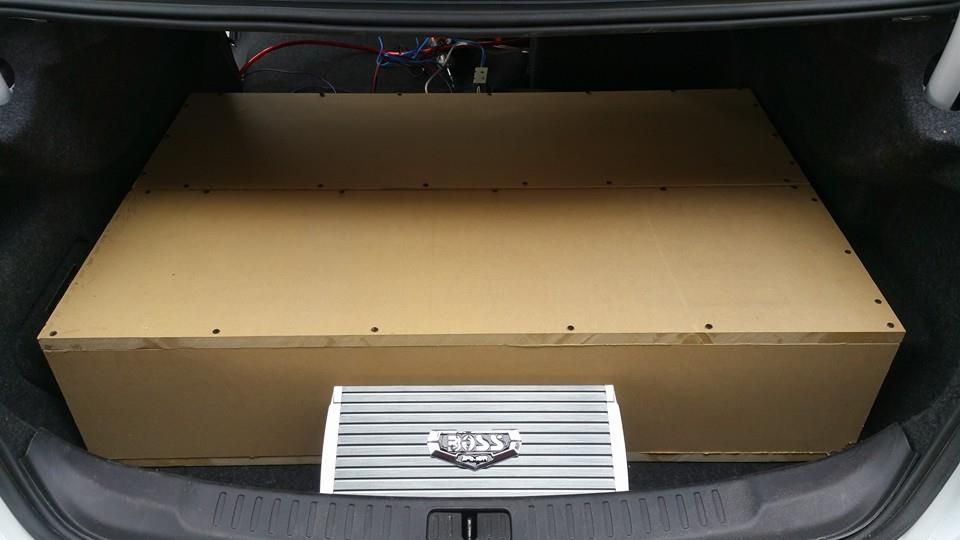 A car trunk with a large wooden speaker box taking up most of the space and an amplifier in front.