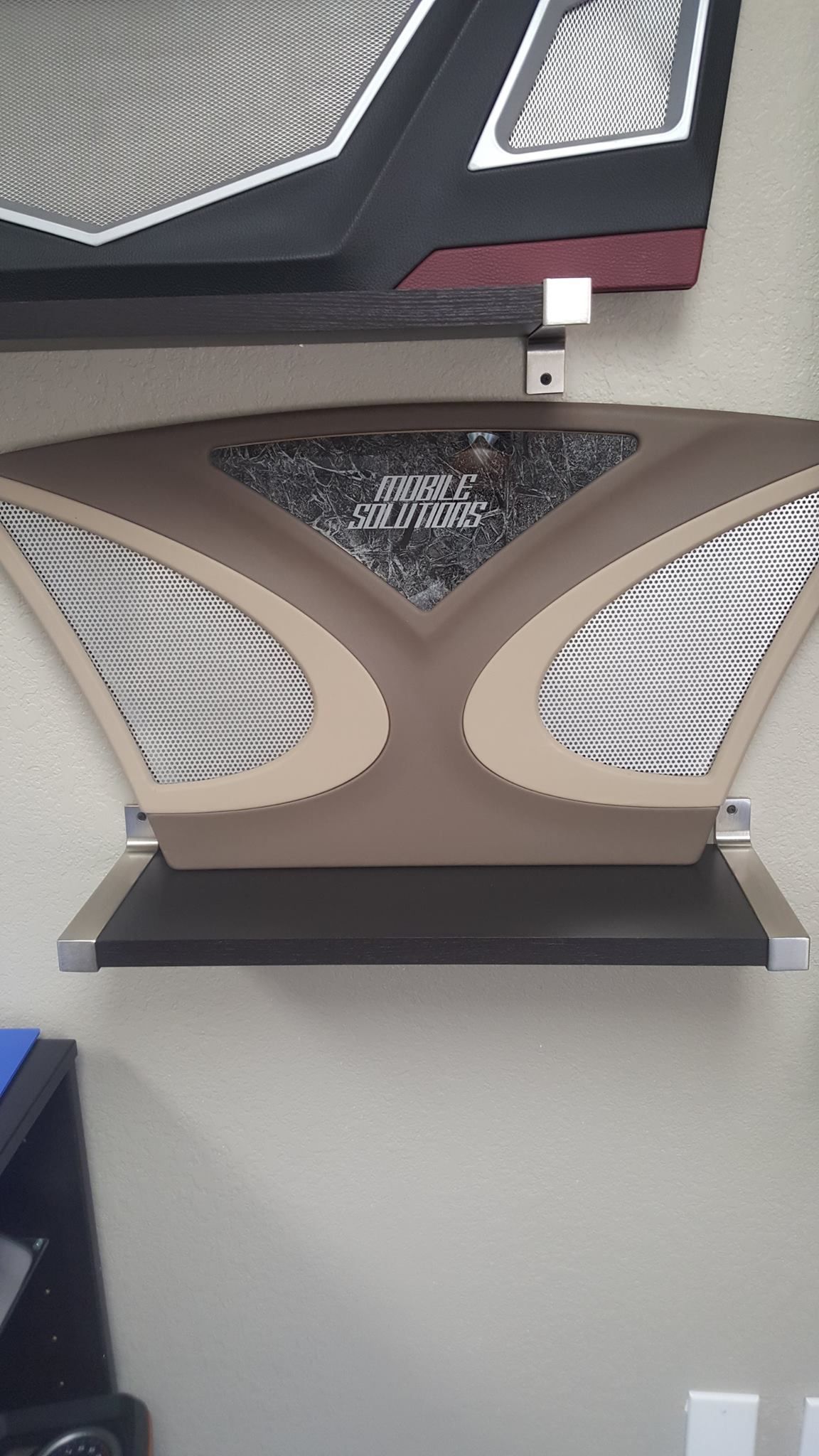 Tan and silver futuristic-looking wall panel with a black shelf beneath it. 