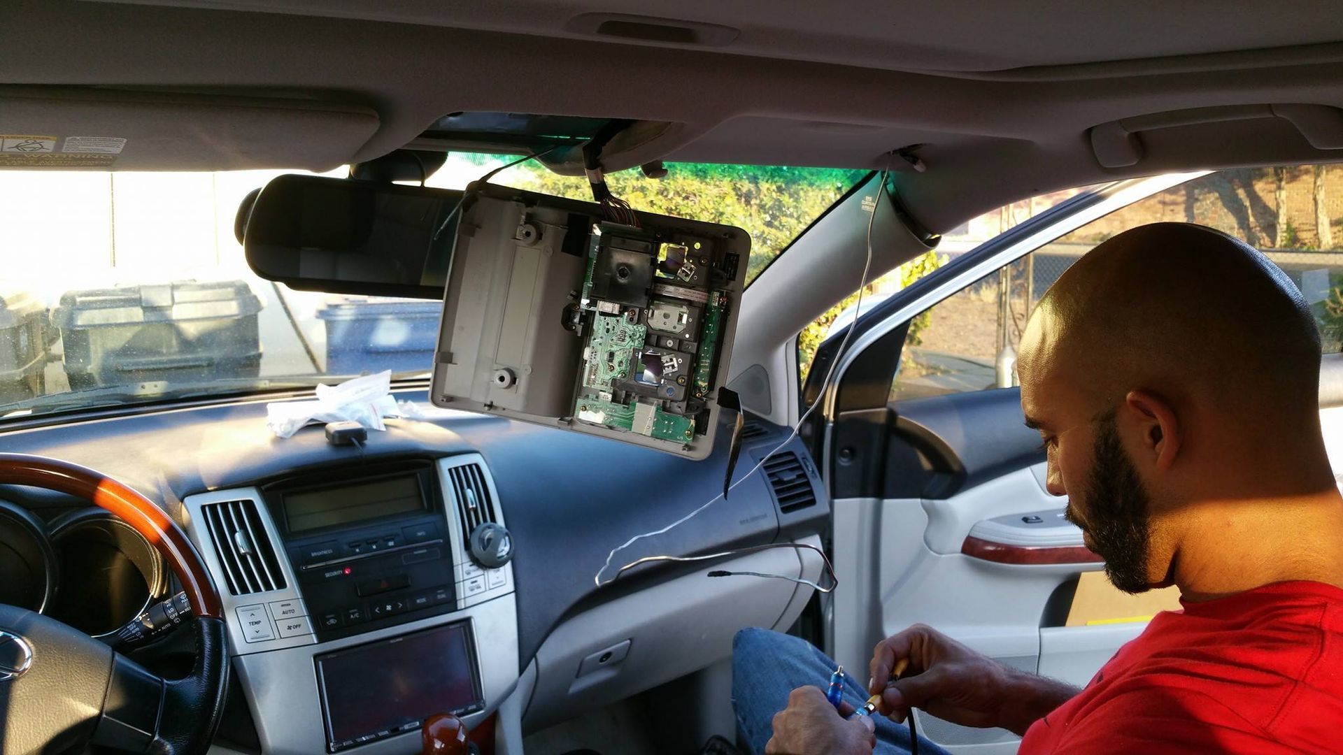 Man working on car electronics, with a dashboard and overhead console open. Interior shot, daytime.