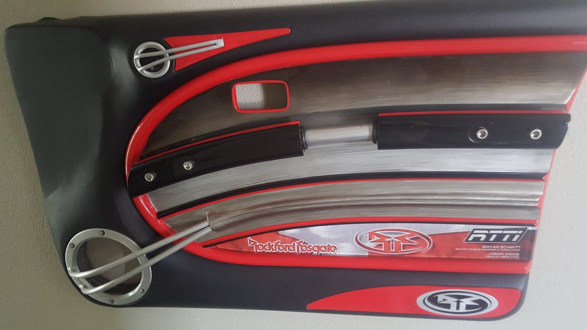 Custom car door panel with black, red, and silver accents, featuring speaker, handle and logo.