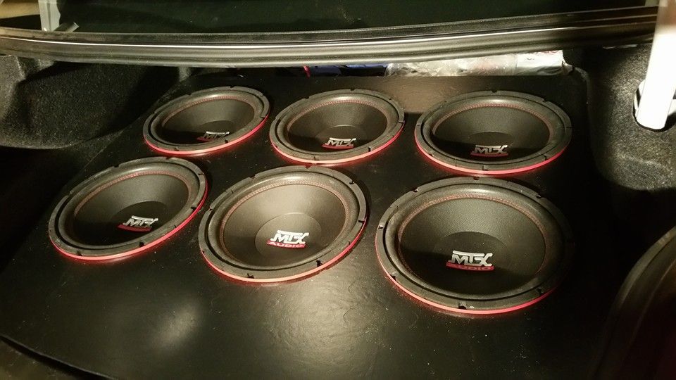Six black subwoofers with red rims installed in the trunk of a car.