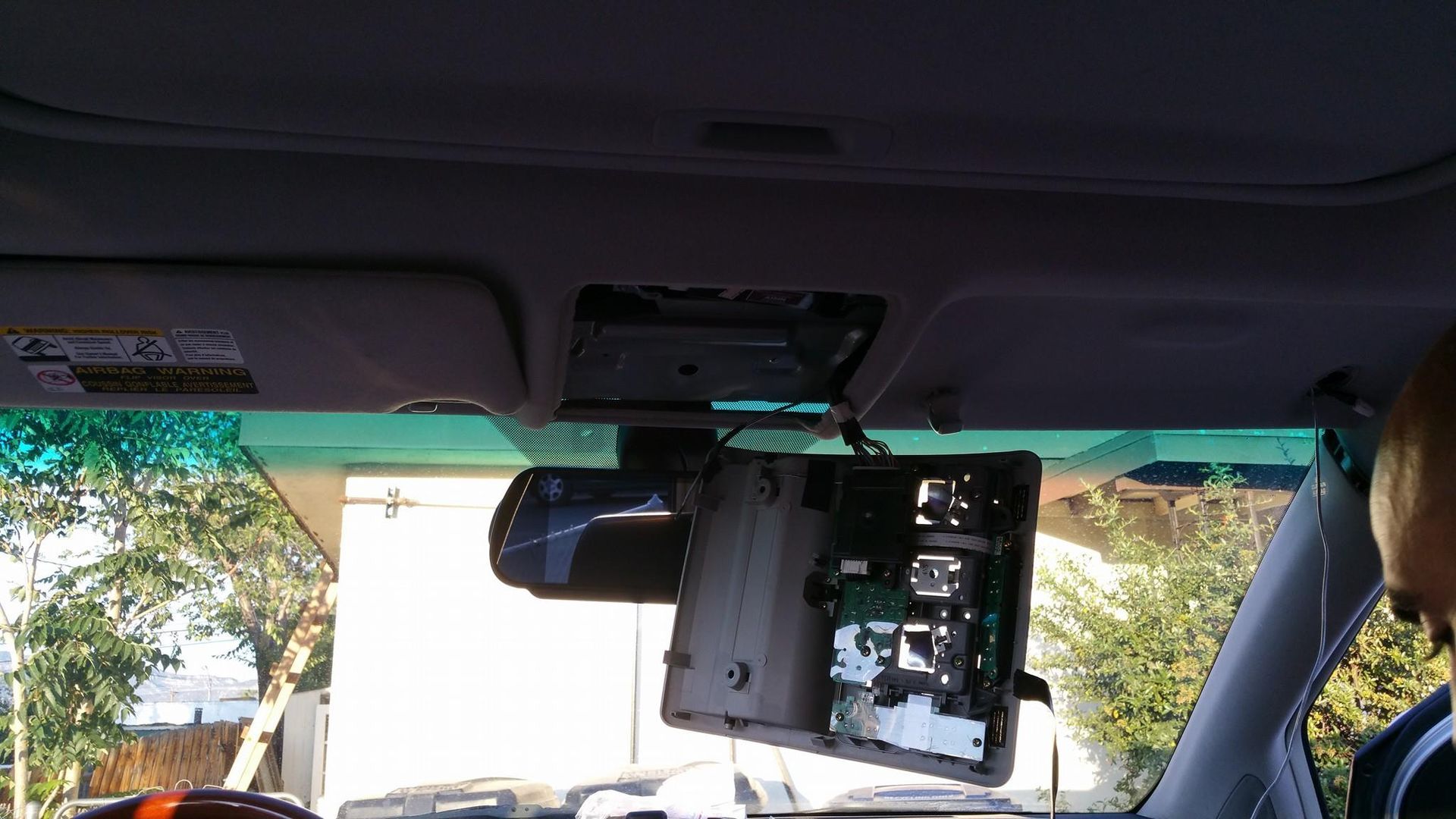 Interior car view with the overhead console disassembled, revealing circuit boards. The dashboard and windshield are visible.