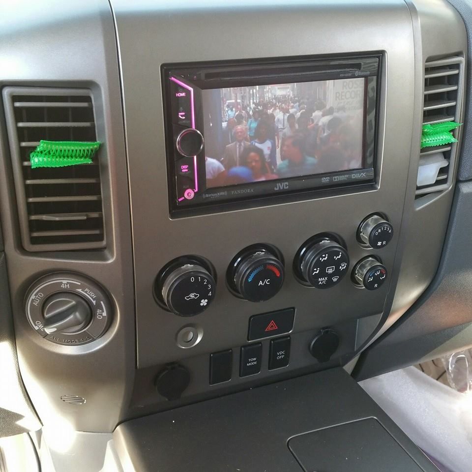 Car dashboard with aftermarket stereo displaying a video; green air fresheners on vents.