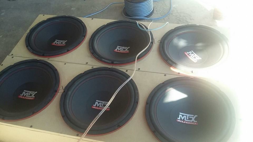 Six black car subwoofers mounted on a wooden board, with LED strip lighting.