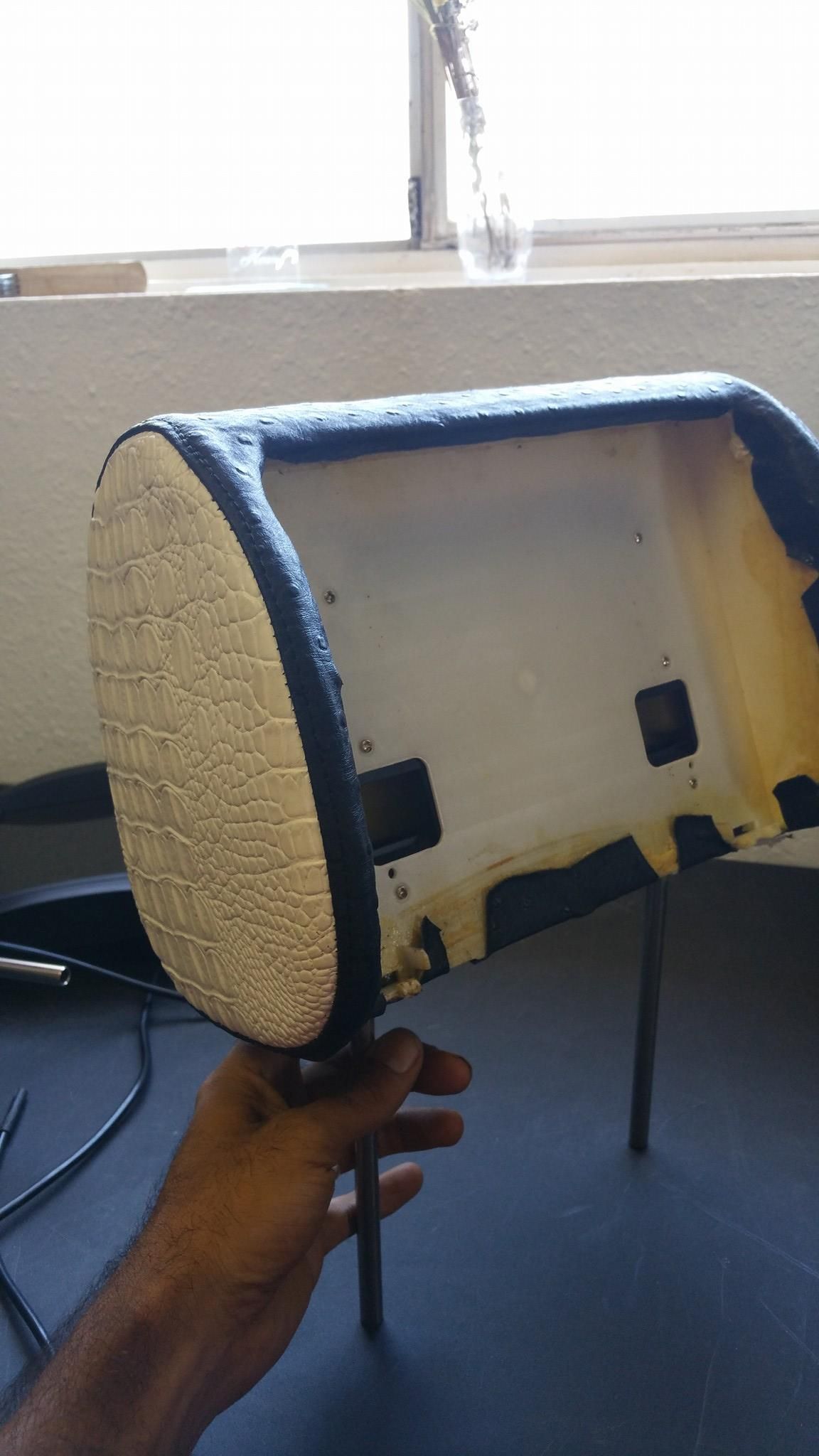 Hand holding a car headrest with a black border and foam padding.