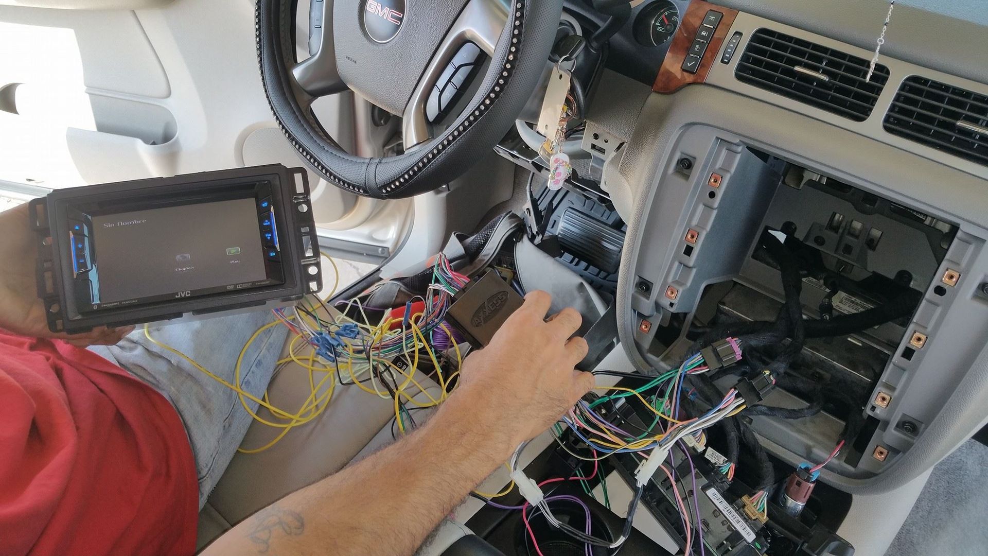 Person installing a car stereo. Interior of a vehicle is visible with the dashboard disassembled and wires exposed.