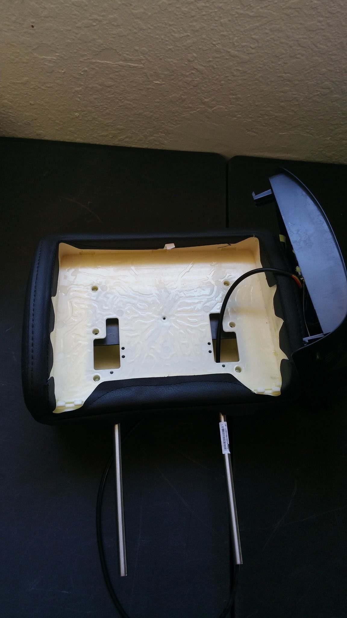 A car headrest with exposed foam and metal posts, partially disassembled.  Black leather and gray accents.