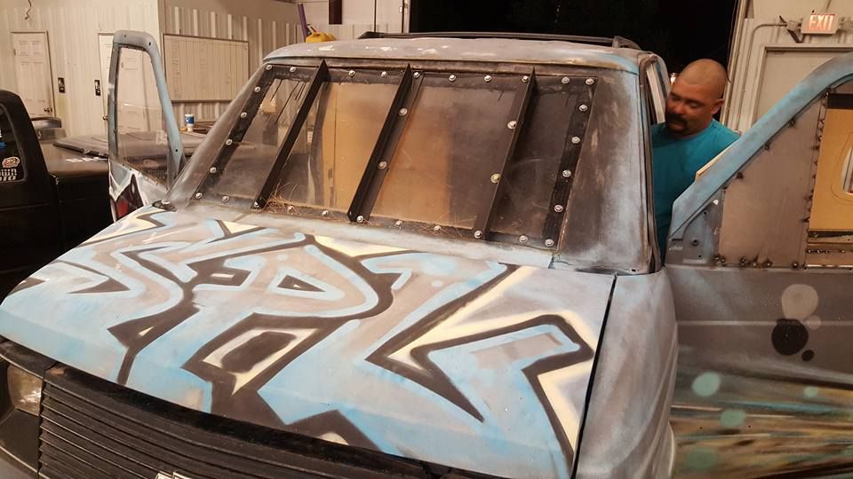 Man working on a custom van with a graffiti design on the hood and a unique window design; he's standing by the open door.