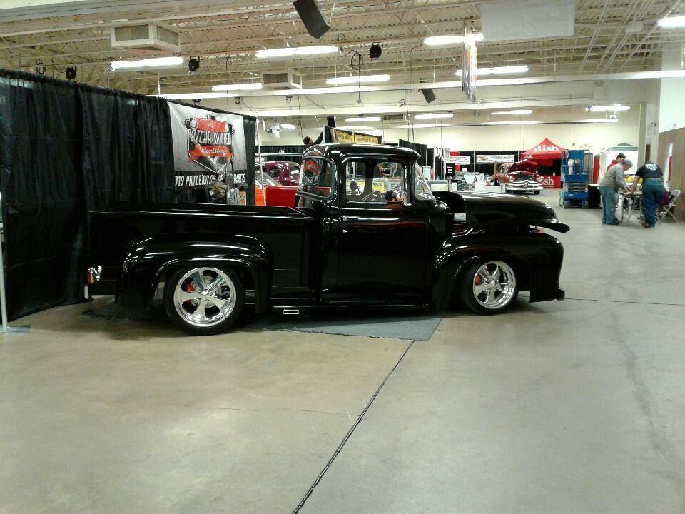 Black classic pickup truck with chrome wheels on display at an indoor auto show.