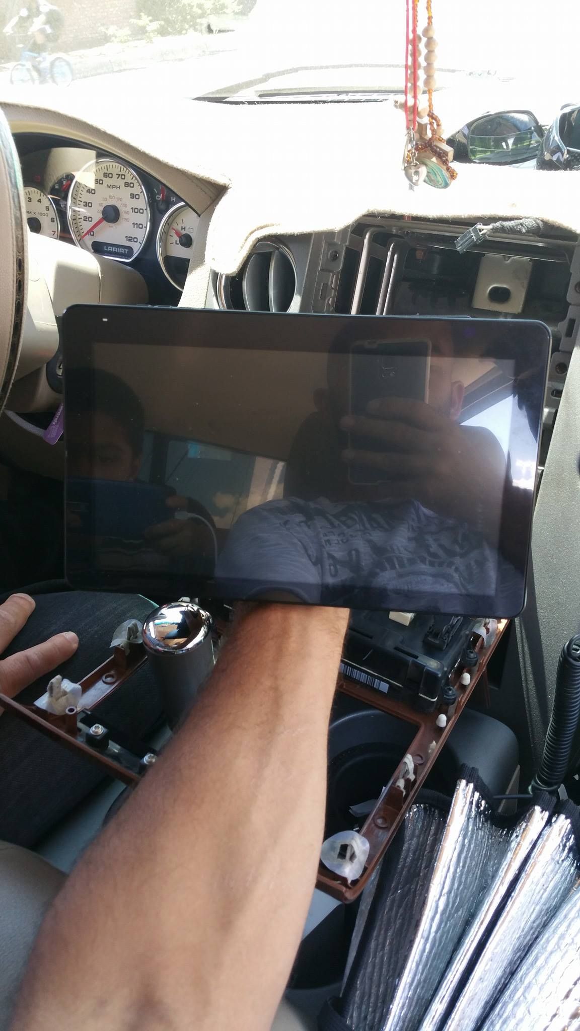 Person holding a large car stereo screen in a disassembled dashboard. Interior car shot, sunny day.