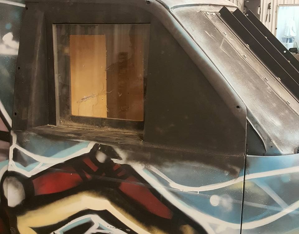 A partially constructed, black-painted vehicle with a window, adorned with graffiti art.