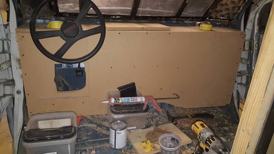 Interior view of a vehicle under construction.  A steering wheel is mounted on a large wooden panel.