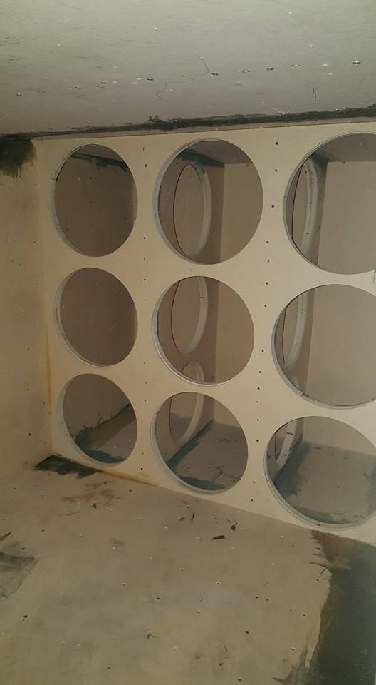 A wooden structure with nine circular openings. The openings appear to be for speaker installation in a built-in enclosure.