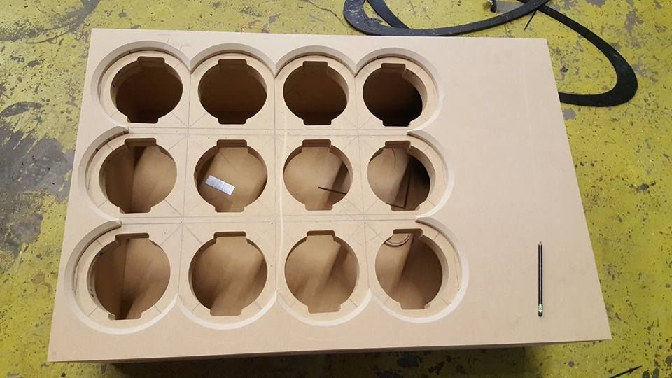 A wooden board with 12 circular cutouts, arranged in three rows, and a slot, likely a custom storage or display piece.