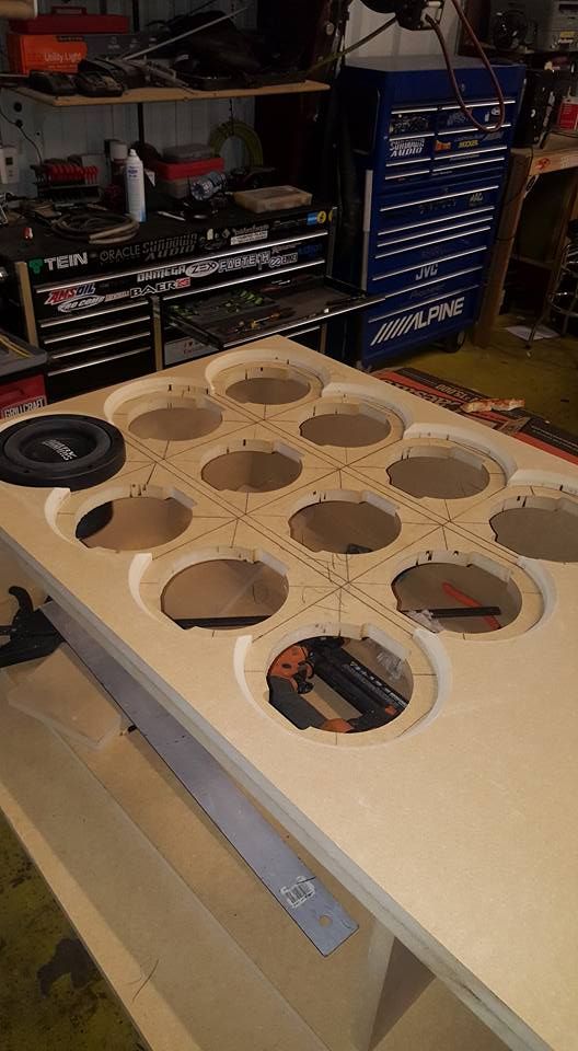 A partially constructed wooden beer pong table with circular cutouts. A toolbox and workshop setting are in the background.