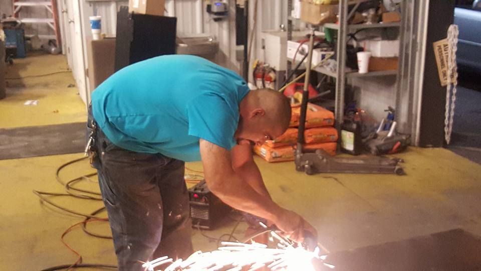 Man in blue shirt using a grinder, creating sparks in a workshop setting.