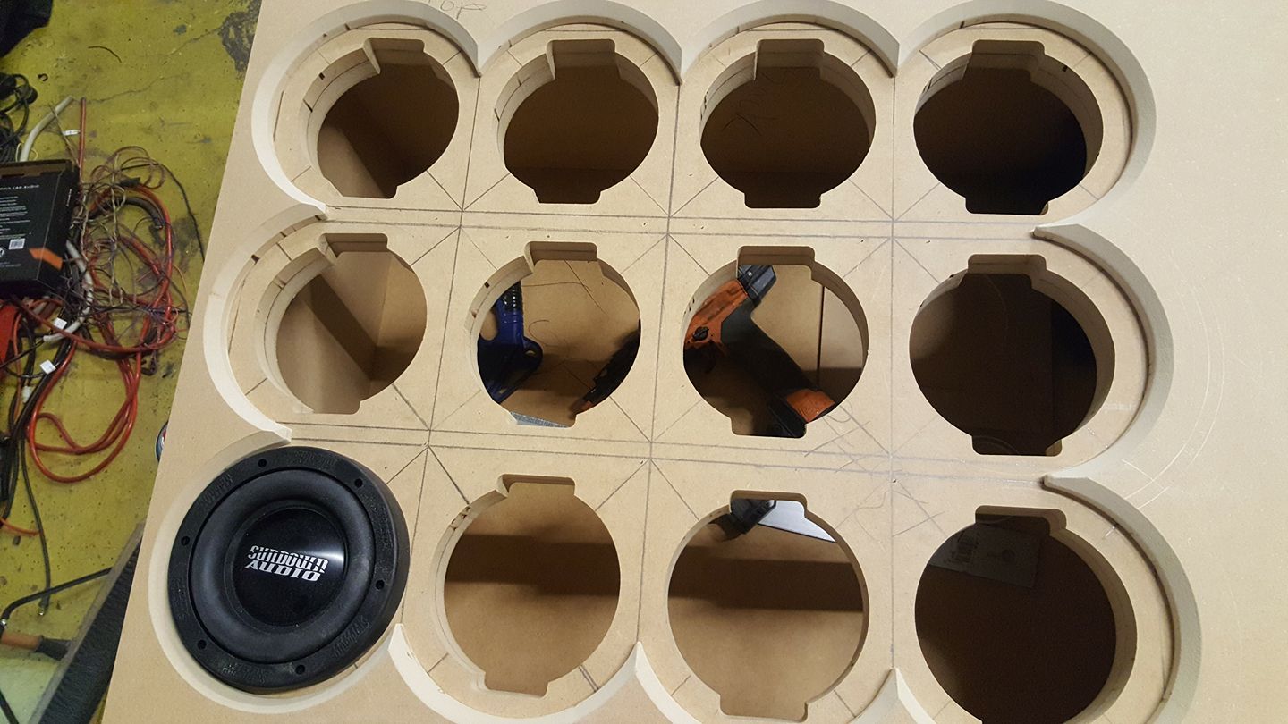 A car audio project with a subwoofer and multiple round speaker cutouts in a wooden board.