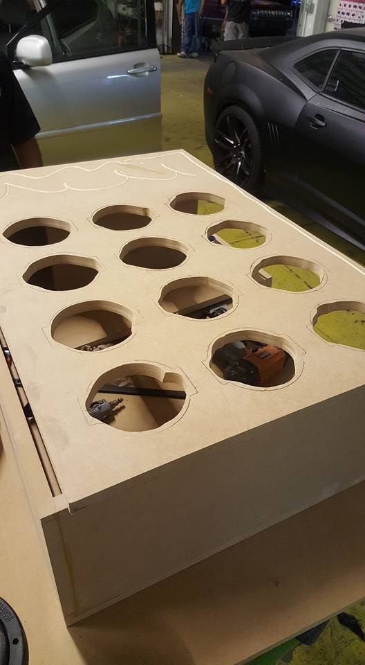 Wooden box with multiple circular openings. Black and brown objects partially fill some holes.