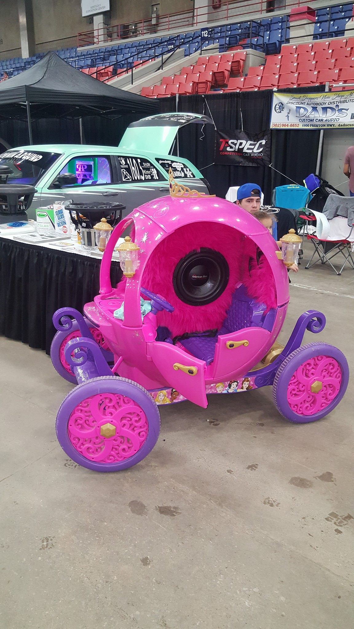 A bright pink Cinderella carriage, with purple wheels and details, on display at an indoor event.