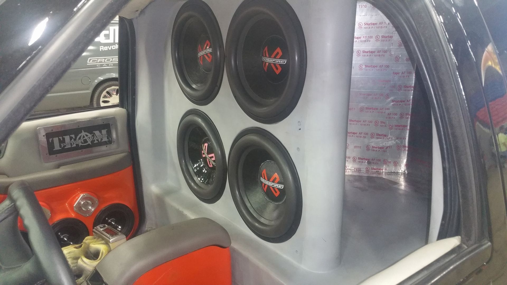 Interior of a car modified with four large subwoofers built into the back wall, gray and red accents.