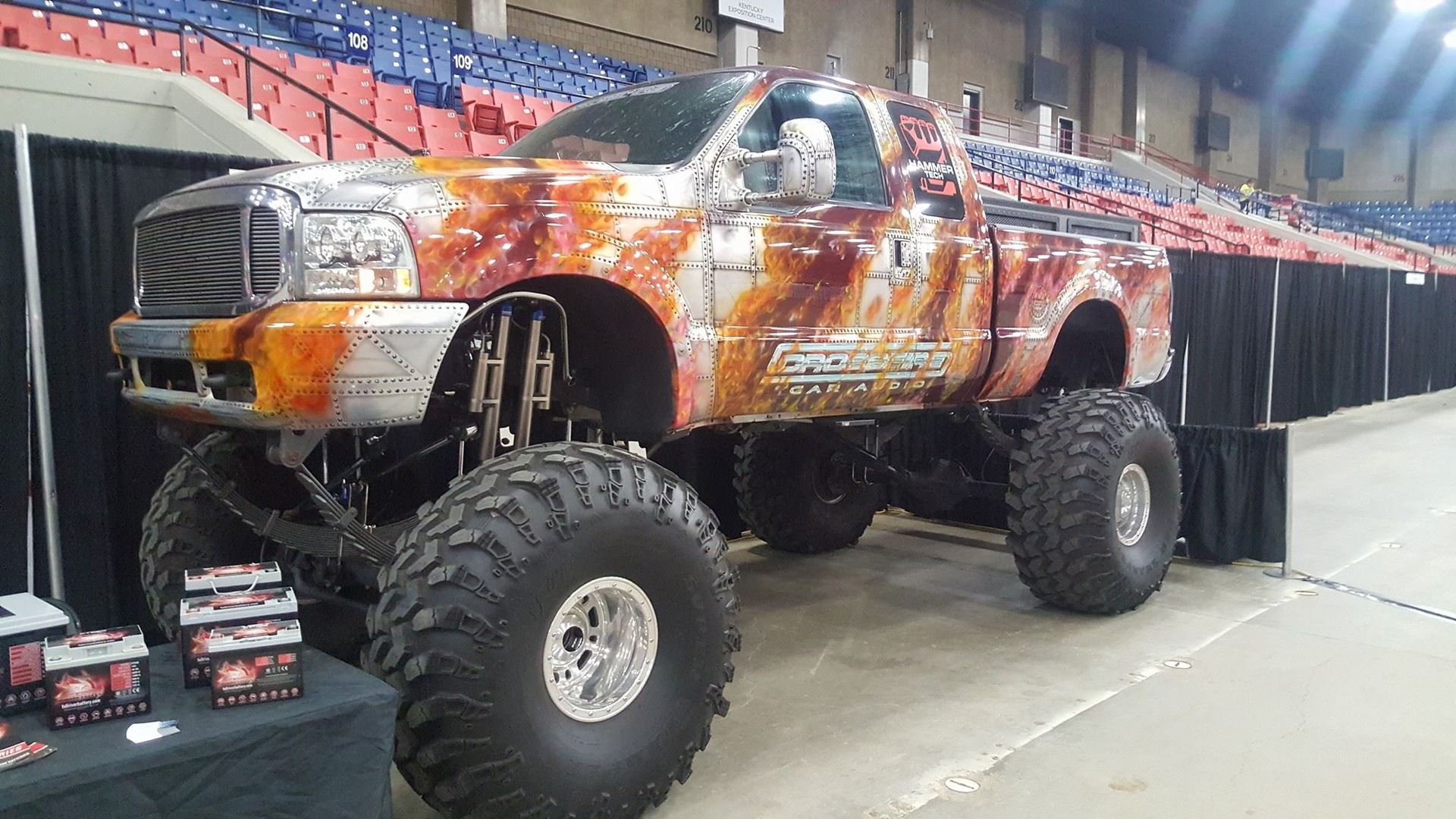 A monster truck with a rusted metal design and enormous tires on display indoors.