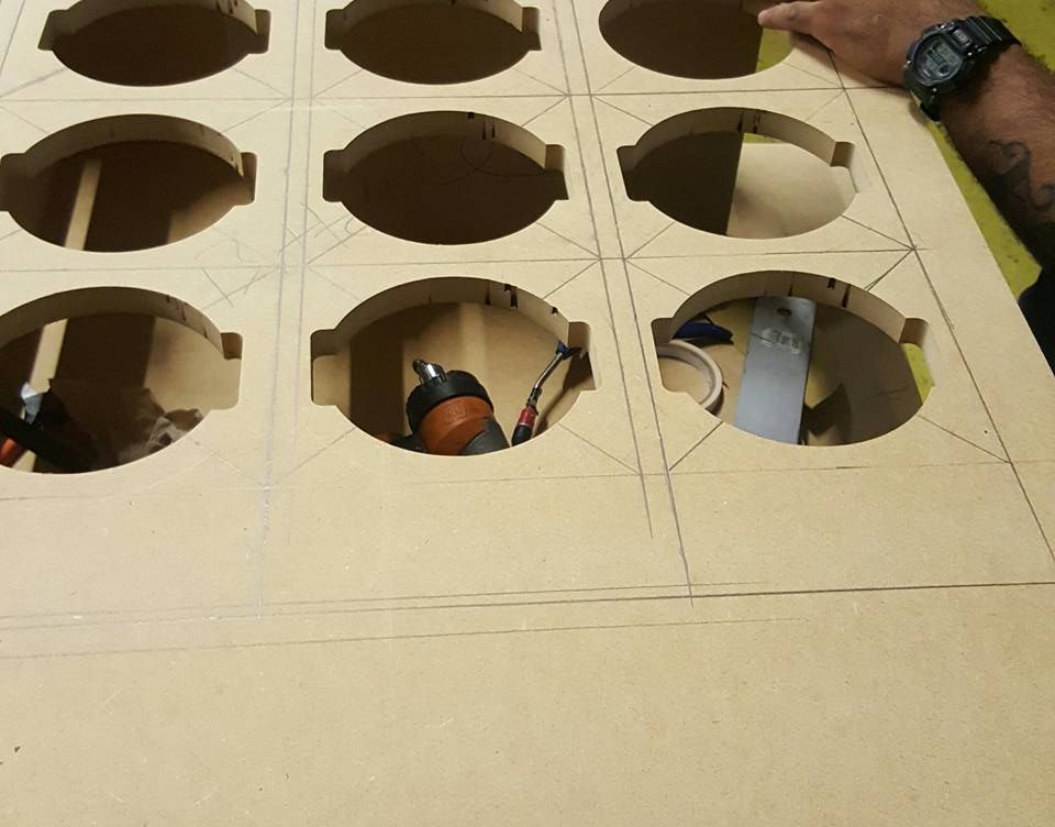 A person's hand near a cut-out board with multiple oval-shaped holes, possibly for an audio setup.