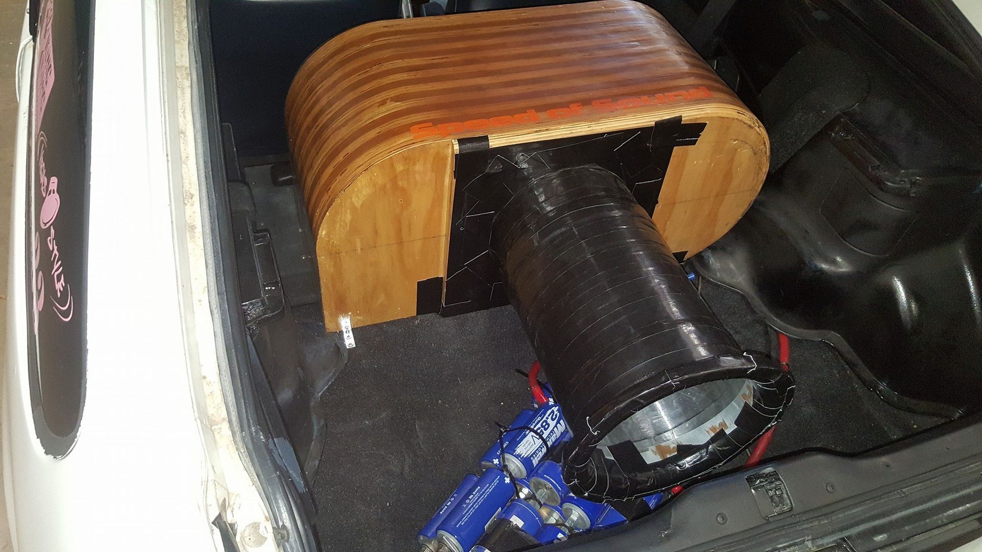 A wooden structure and black tube inside a car trunk, with wires and a toy car visible.