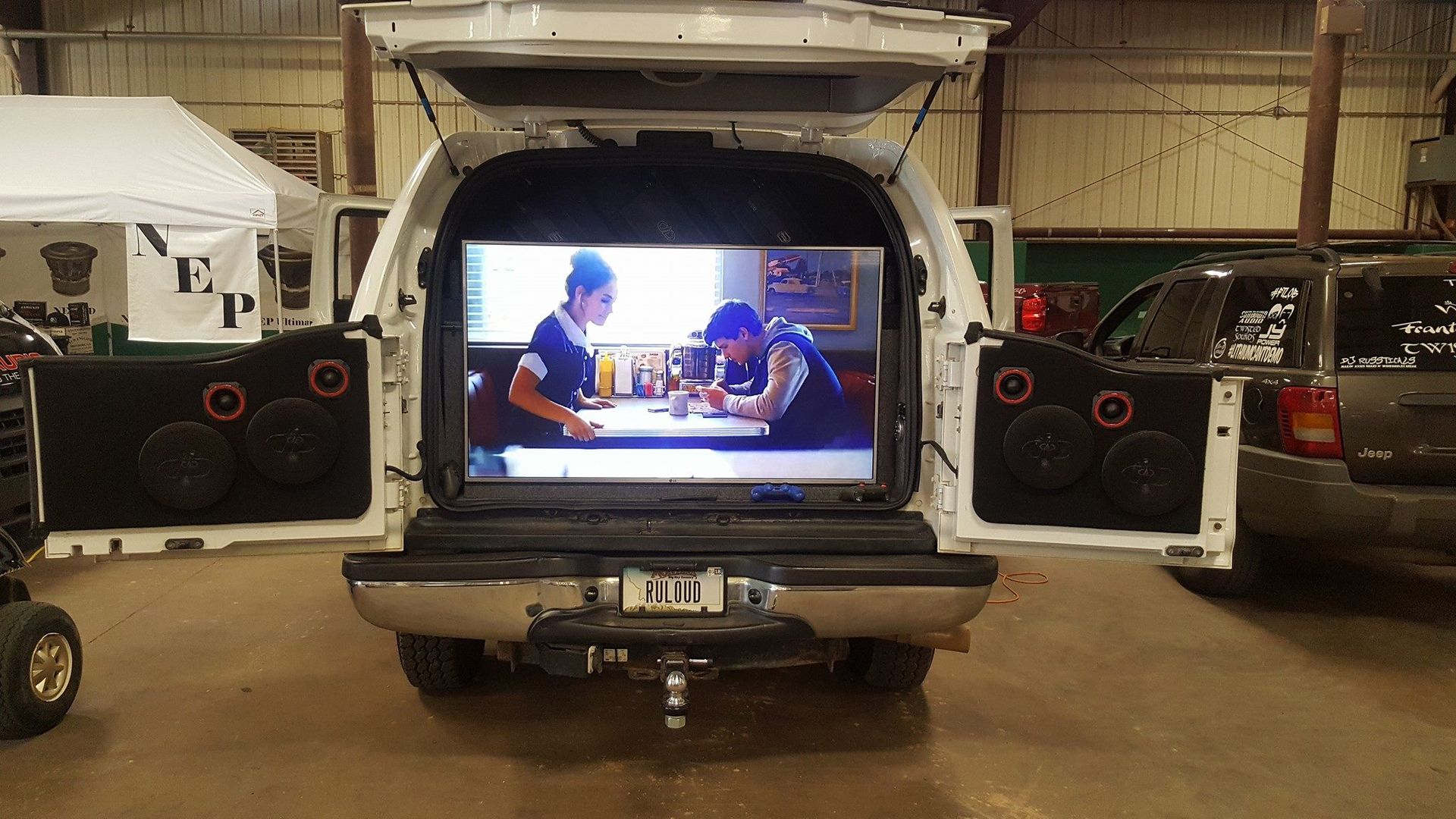 White pickup truck's open trunk displays a large screen showing a video.