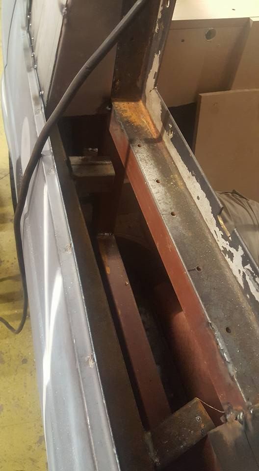Interior view of a rusty metal industrial machine with red and gray surfaces. A black cable runs along the left.