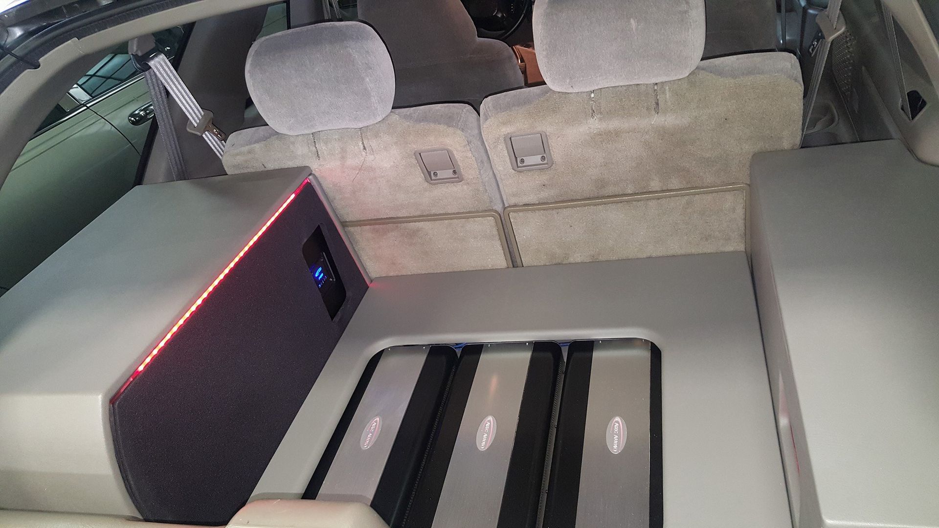 Back of a vehicle modified with audio equipment, including amplifiers and speakers, lit with red and blue lights.