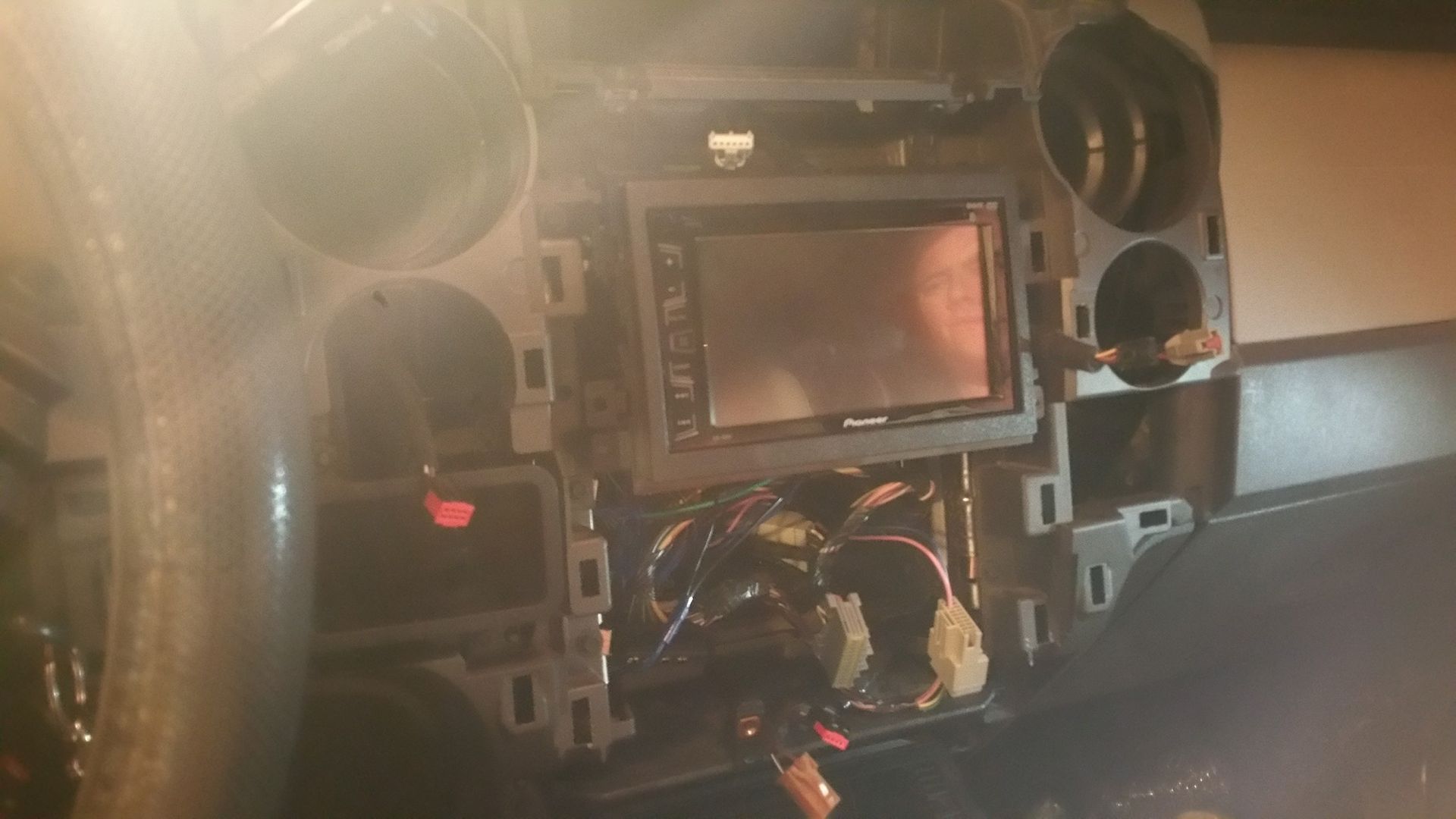 Car dashboard with a removed stereo; wires are exposed. The setting appears to be a garage.