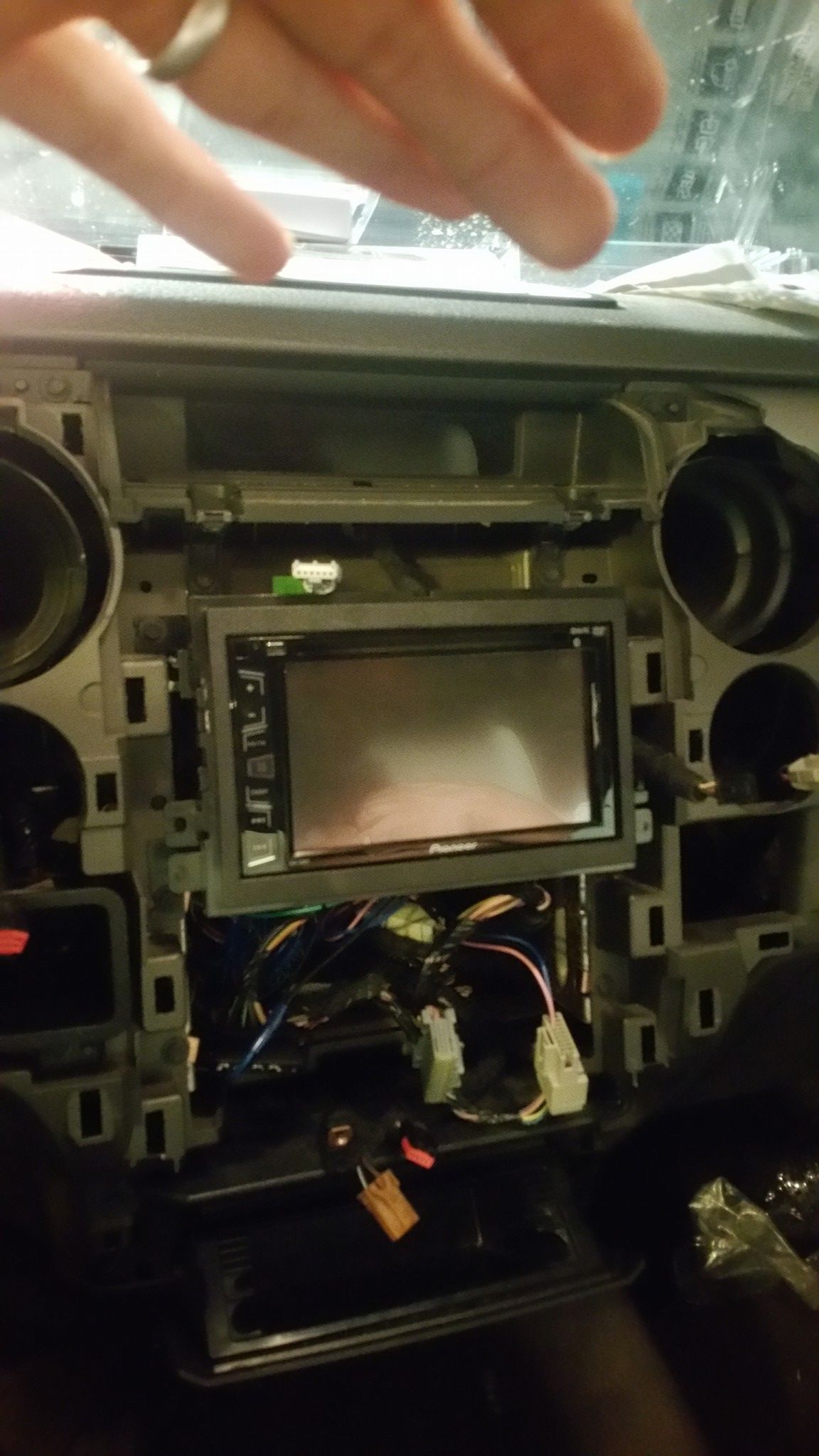 Car dashboard with aftermarket stereo installed, wires visible. Hand pointing at the stereo.