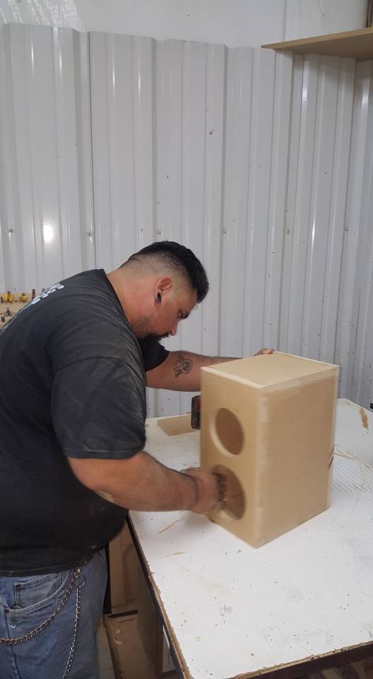 Man building a speaker box with two circular holes. He is standing at a workbench in a workshop.