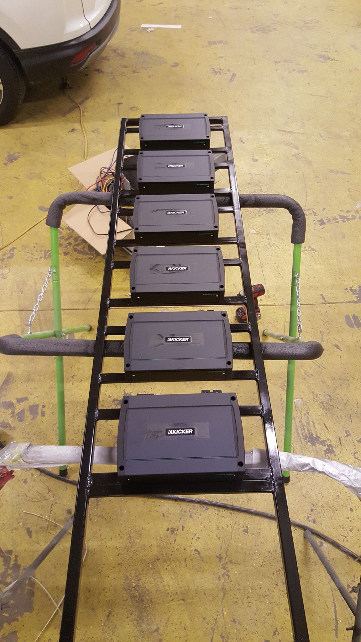 Six black amplifiers are mounted on a ladder-like frame in a workshop setting.