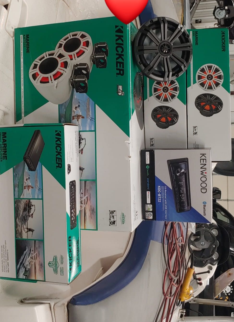 Boxes of Kicker and Kenwood marine audio equipment on a boat, including speakers, a receiver, and an amplifier.