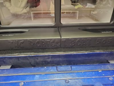 Two car audio speaker units with lettering and a reflective blue surface below.