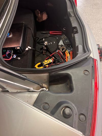 Open car trunk with electrical equipment and tools; silver car exterior.