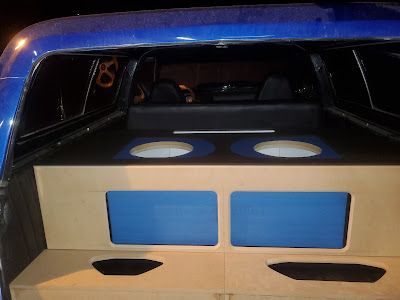 Blue car interior with custom subwoofer enclosure. The enclosure is light brown and features two large speaker holes.