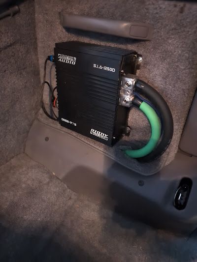 Black car audio amplifier installed in a vehicle's trunk, with thick power cables connected.