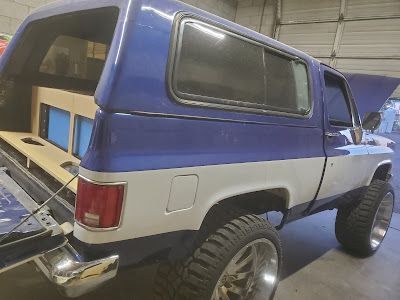 A lifted blue and white Chevrolet Blazer with its tailgate open, revealing a wooden structure inside.