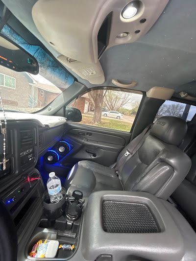 Interior view of a truck cabin with grey seats, a center console, and a water bottle. The speaker glows blue.