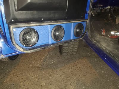 Blue car door with three black speaker grills installed. The setting appears to be a garage or workshop.