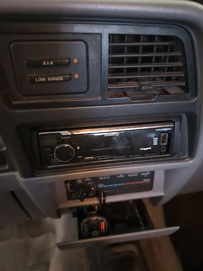 Dashboard of a vehicle with a radio, vents, and controls for 4x4 and low range. There's an open storage compartment below.
