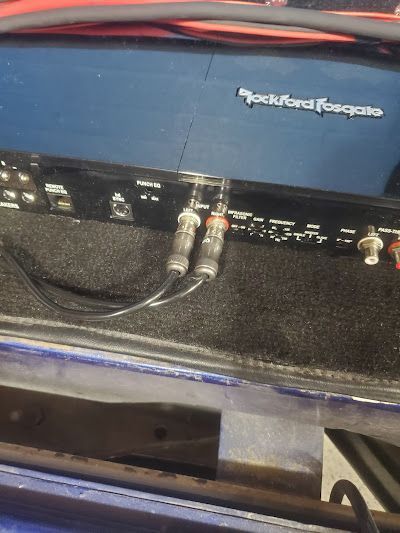 Rear view of a Rockford Fosgate amplifier with two audio cables plugged into it. Black and blue.