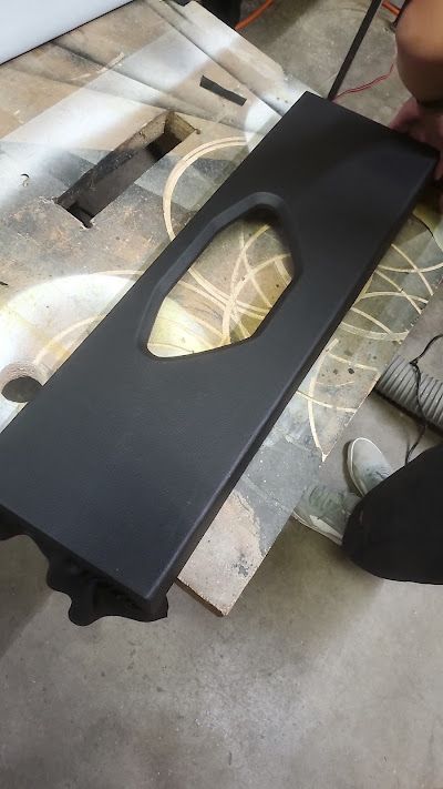Black, rectangular car interior panel with an oval cutout, resting on a wooden surface.