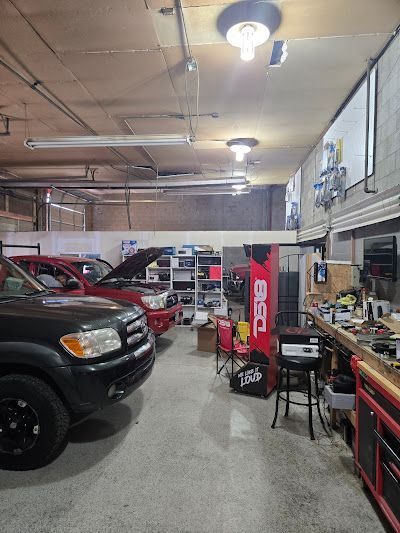 A garage with two trucks, a workbench, tools, and shelving. The space is well lit with fluorescent and overhead lights.