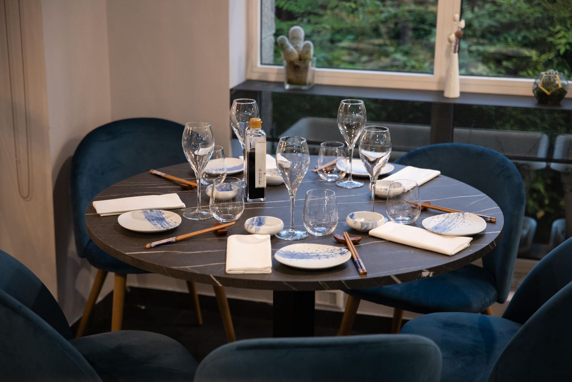 Un tavolo rotondo con piatti, bicchieri, bacchette e una bottiglia di vino.