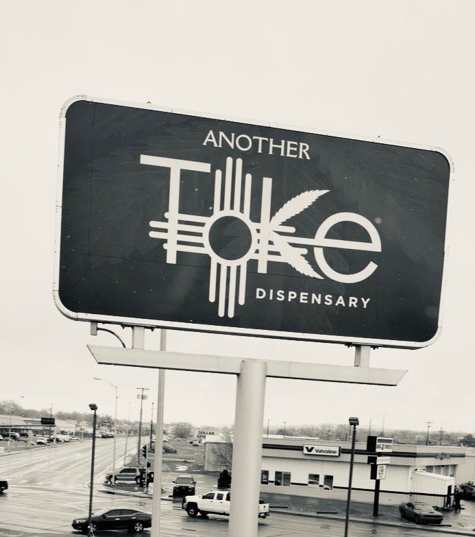 Another Toke Dispensary - Sign on top of building. White metal border, with white logo, dark green background.