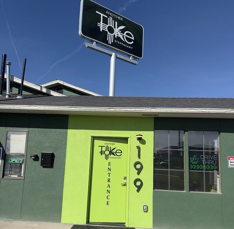 Another Toke Dispensary - Light Green Front Entrance with 199 on the side, the rest of the building is dark green with some windows indicating a drive thru.